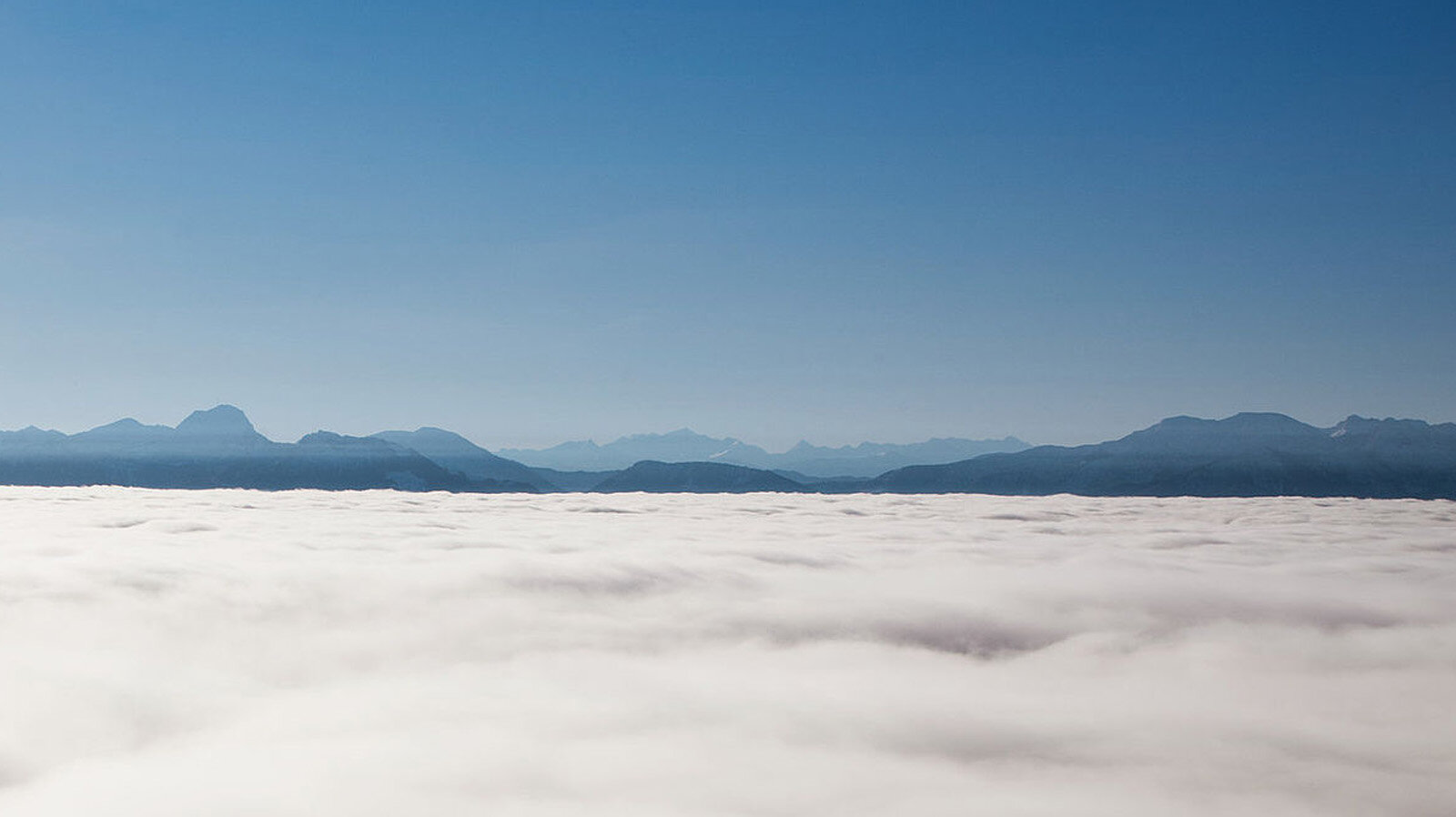 Eine geschlossene Wolkendecke vor einem Gebirge unter blauem Himmel Eine geschlossene Wolkendecke vor einem Gebirge unter blauem Himmel