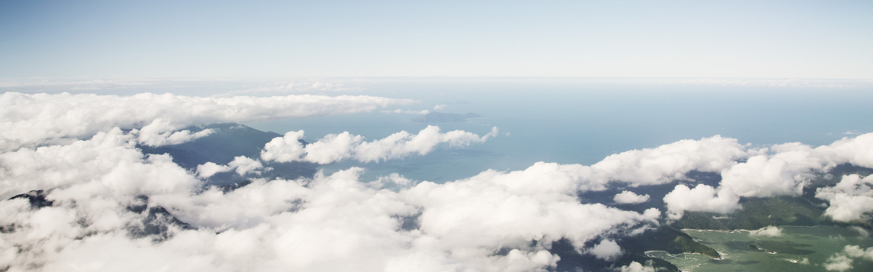 Eine fliegende Boeing 747 über Wolkenformationen mit drunterliegender Küste und Ozean