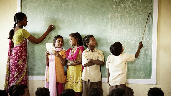 Ein indisches Klassenzimmer, vier Kinder und die Lehrerin vor der Schultafel Ein indisches Klassenzimmer, vier Kinder und die Lehrerin vor der Schultafel